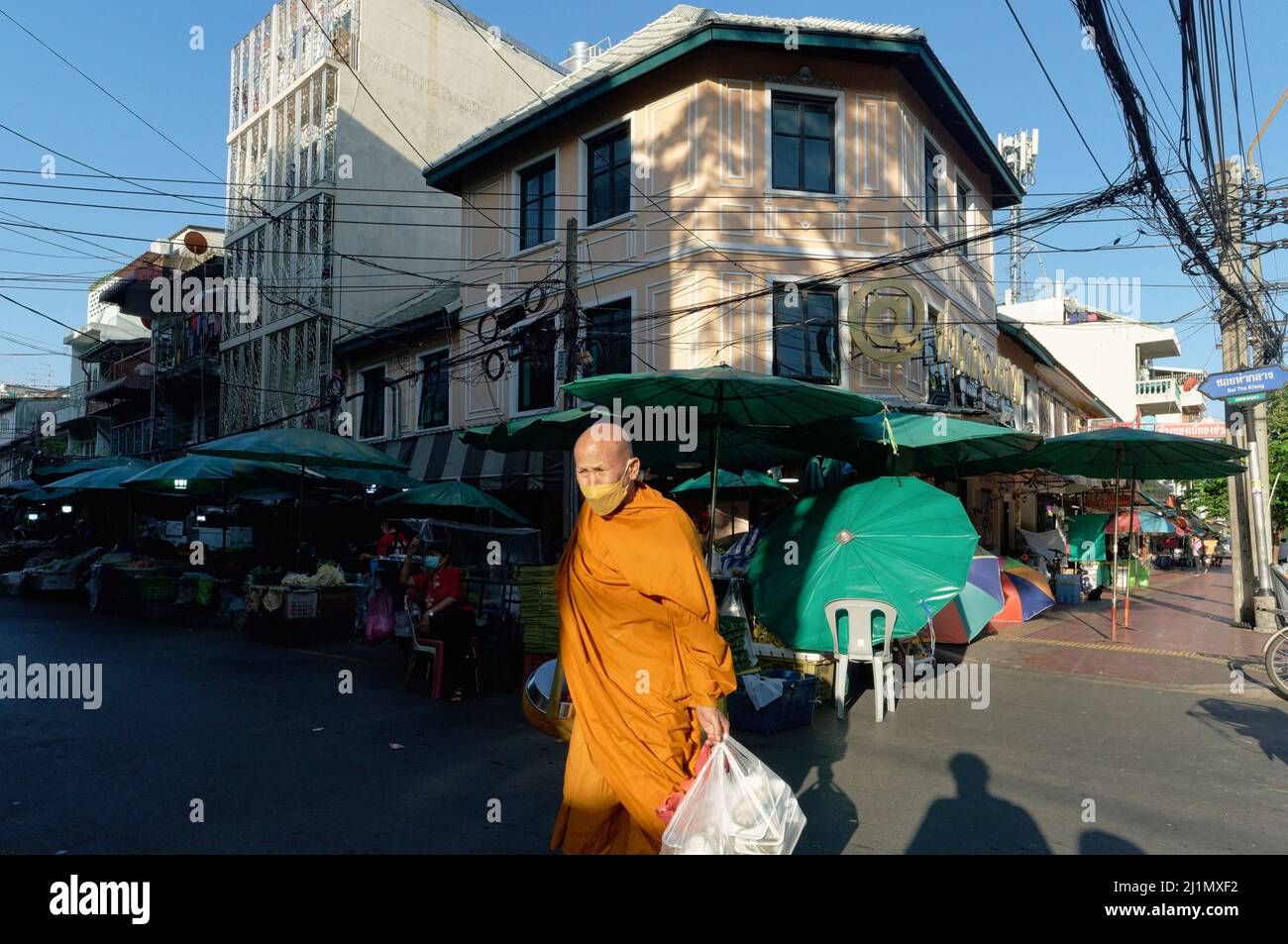 Im frühen Morgenlicht spaziert ein buddhistischer Mönch eine Straße auf dem Pak Klong Talat (Markt) in Bangkok, Thailand, mit einer Tasche voller gesammelter Almosen (Lebensmittel) Stockfoto