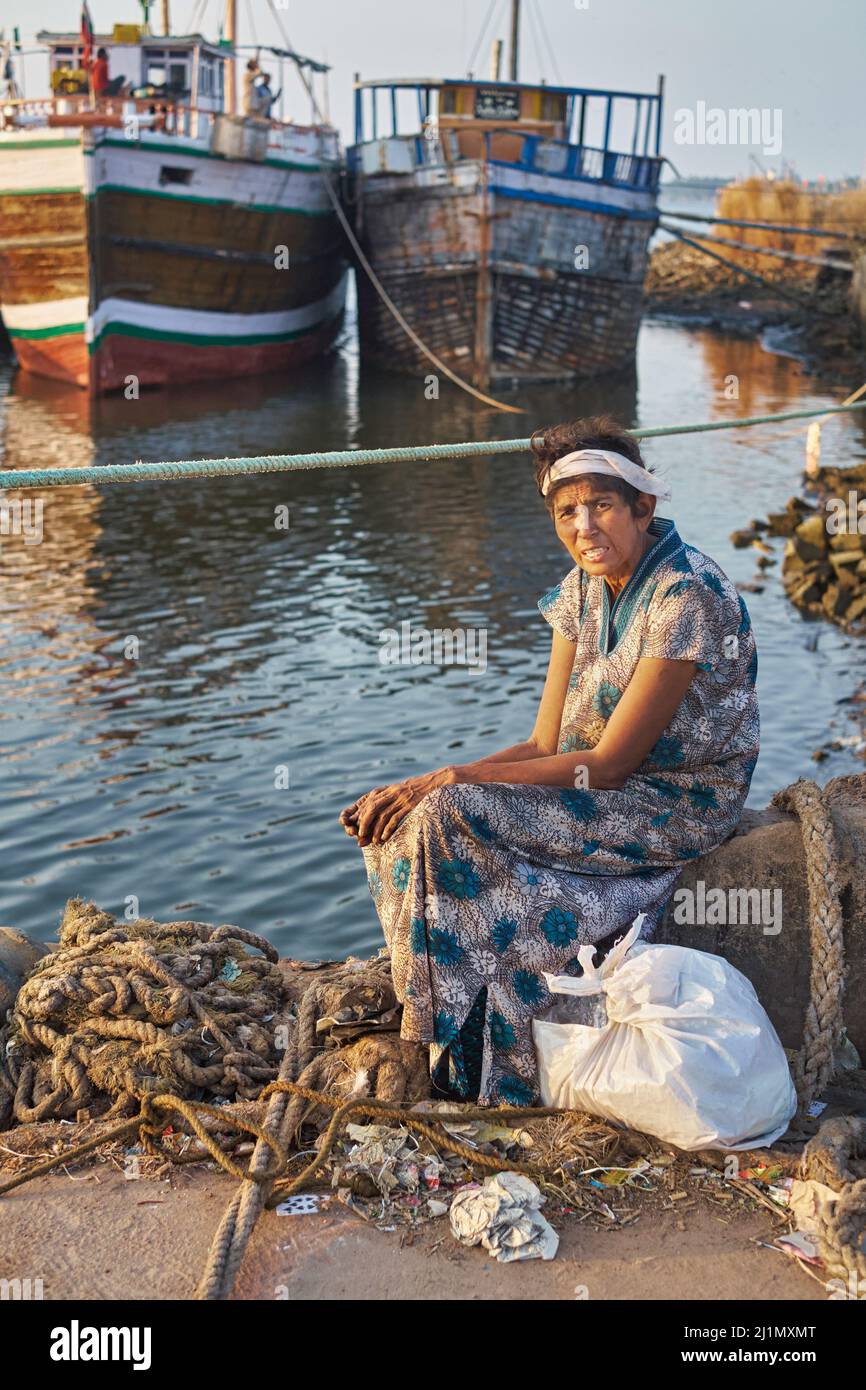 Eine Inderin mittleren Alters sitzt allein in einer weit entfernten Ecke des Alten Hafens in Mangalore (Mangaluru), Karnataka, Südindien, und fischt Boote im b/g Stockfoto
