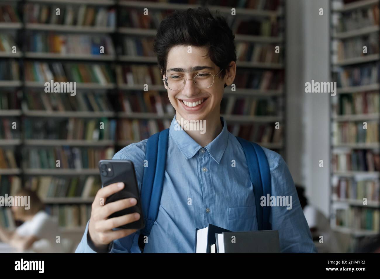 Teenager mit Brille und Smartphone in der Universitätsbibliothek Stockfoto