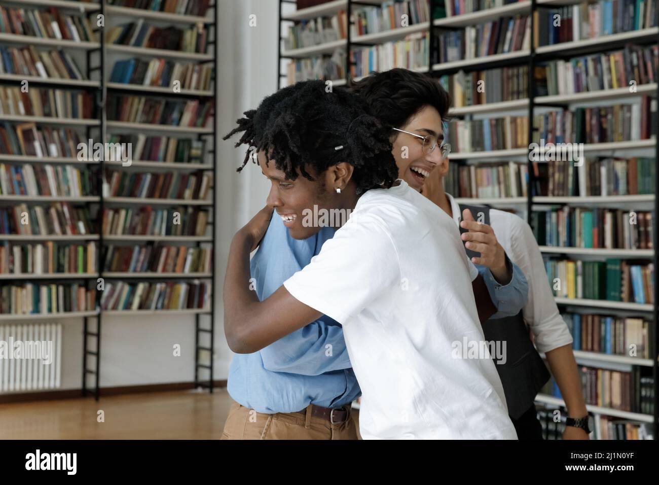 Glückliche multiethnische Teenager Studenten umarmen stehen in der Bibliothek Stockfoto