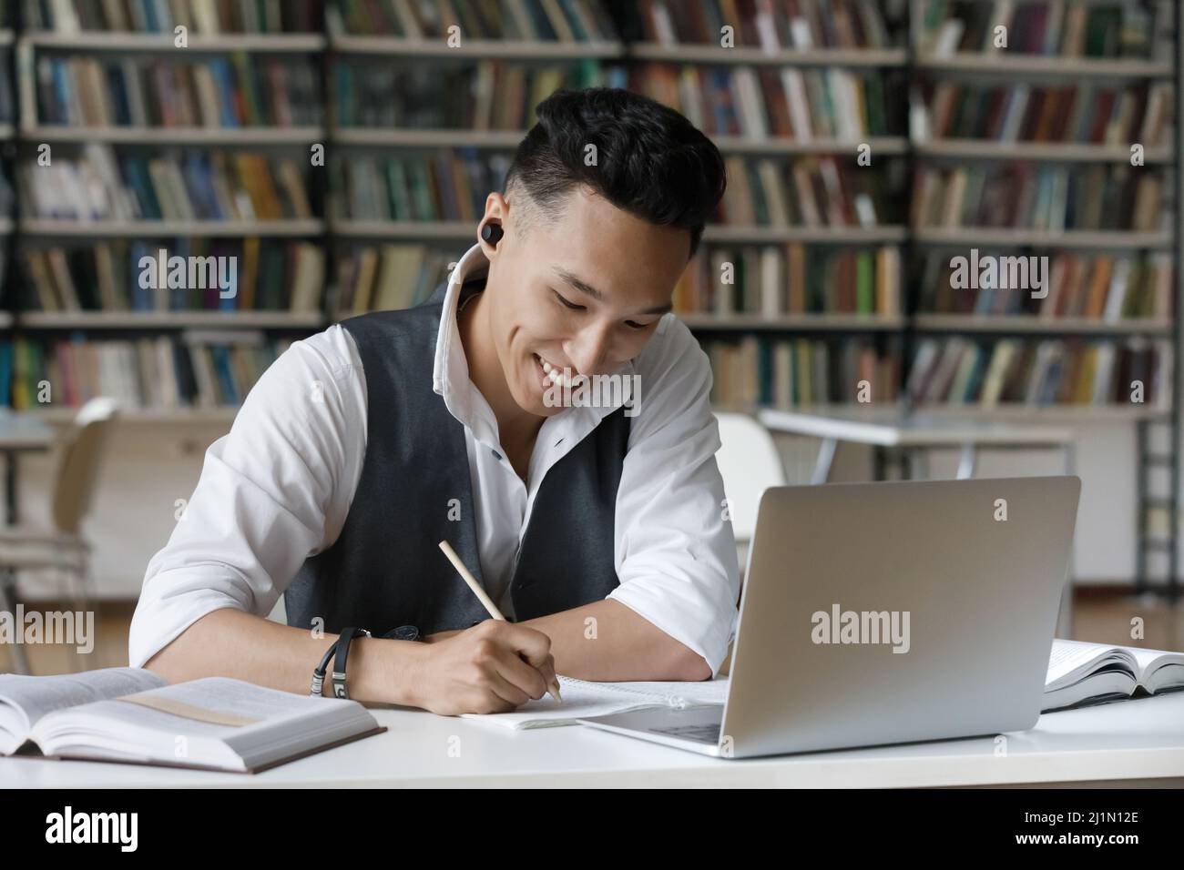 Asian Kerl nehmen Notizen im Copybook während des Studiums in der Bibliothek Stockfoto