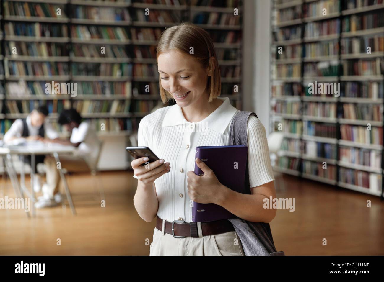 Junge attraktive Student Mädchen in der Bibliothek mit Smartphone stehen Stockfoto