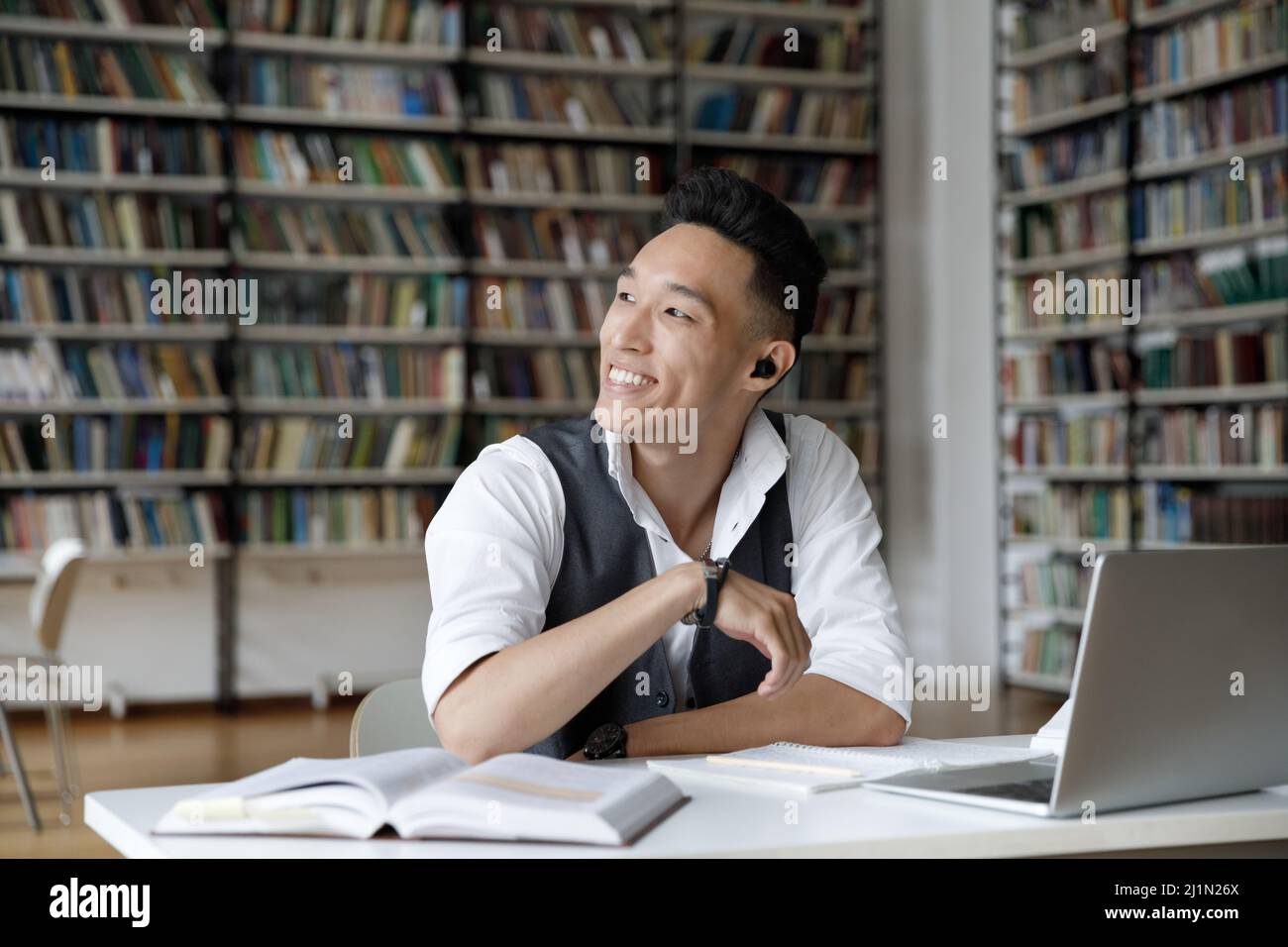 Lächelnder Koreaner sitzt am Tisch und studiert in der Bibliothek Stockfoto