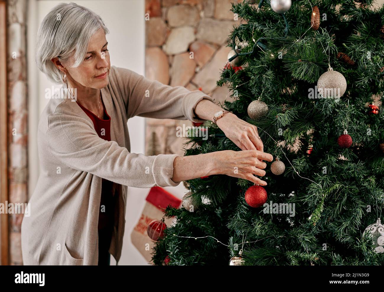 Ihr könnt gleich hier hingehen. Eine kurze Aufnahme einer sorglosen, reifen Frau, die tagsüber Dekorationen auf einen Weihnachtsbaum zu Hause legt. Stockfoto