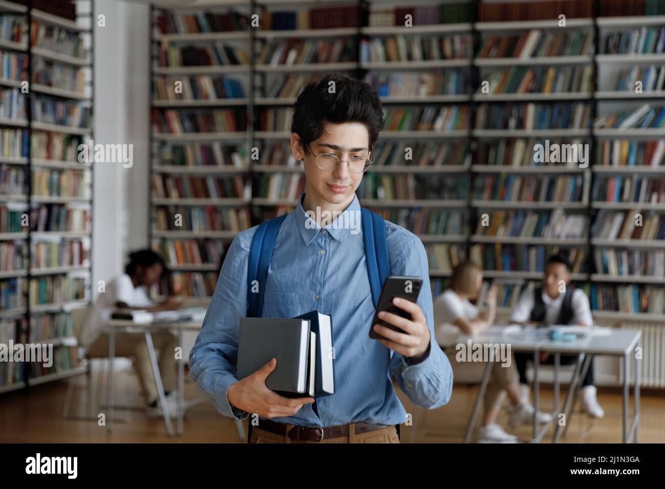 Studenten Kerl mit Arbeitsbüchern und Smartphone in der Bibliothek stehen Stockfoto