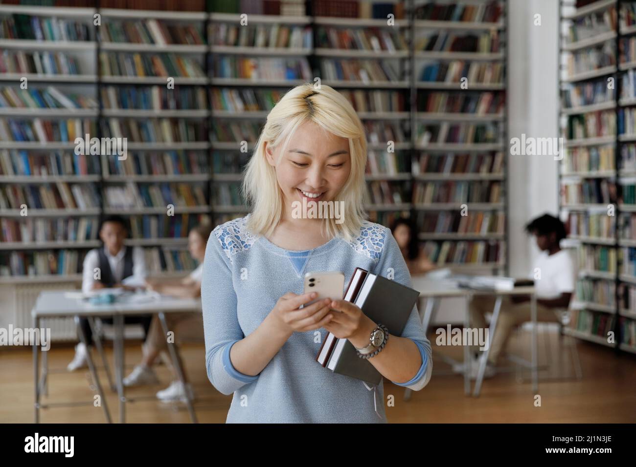 Asiatische Student Mädchen verwenden Smartphone stehen in der Bibliothek mit Arbeitsbüchern Stockfoto