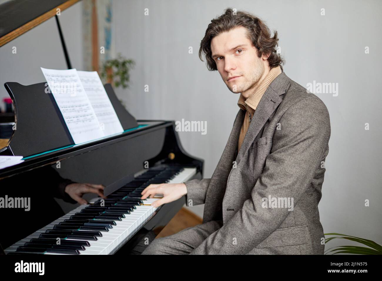 Porträt eines professionellen Pianisten im Anzug, der die Kamera anschaut, während er in der Musikschule auf dem Klavier Notizen spielt Stockfoto