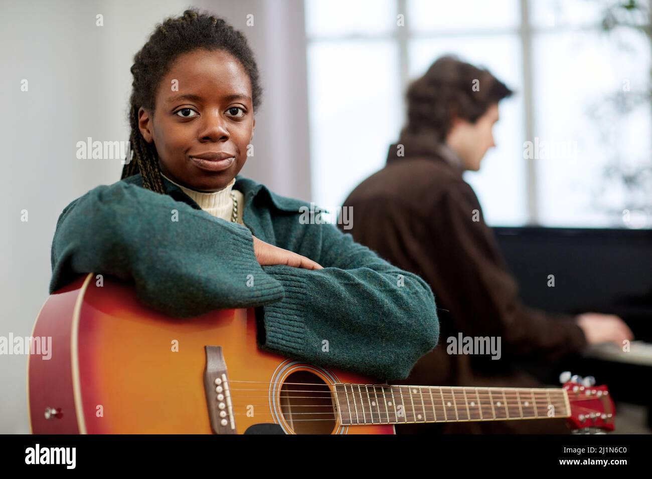 Porträt einer jungen afrikanischen Frau, die mit Gitarre sitzt und die Kamera anschaut, an der Musikschule studiert und das Musizieren von Musikinstrumenten lernt Stockfoto