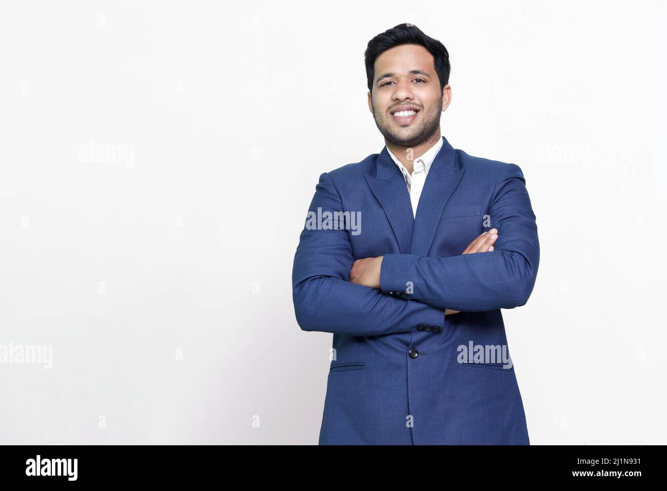 Junger hispanischer Geschäftsmann mit überkreuzten Armen lächelnd. Stockfoto