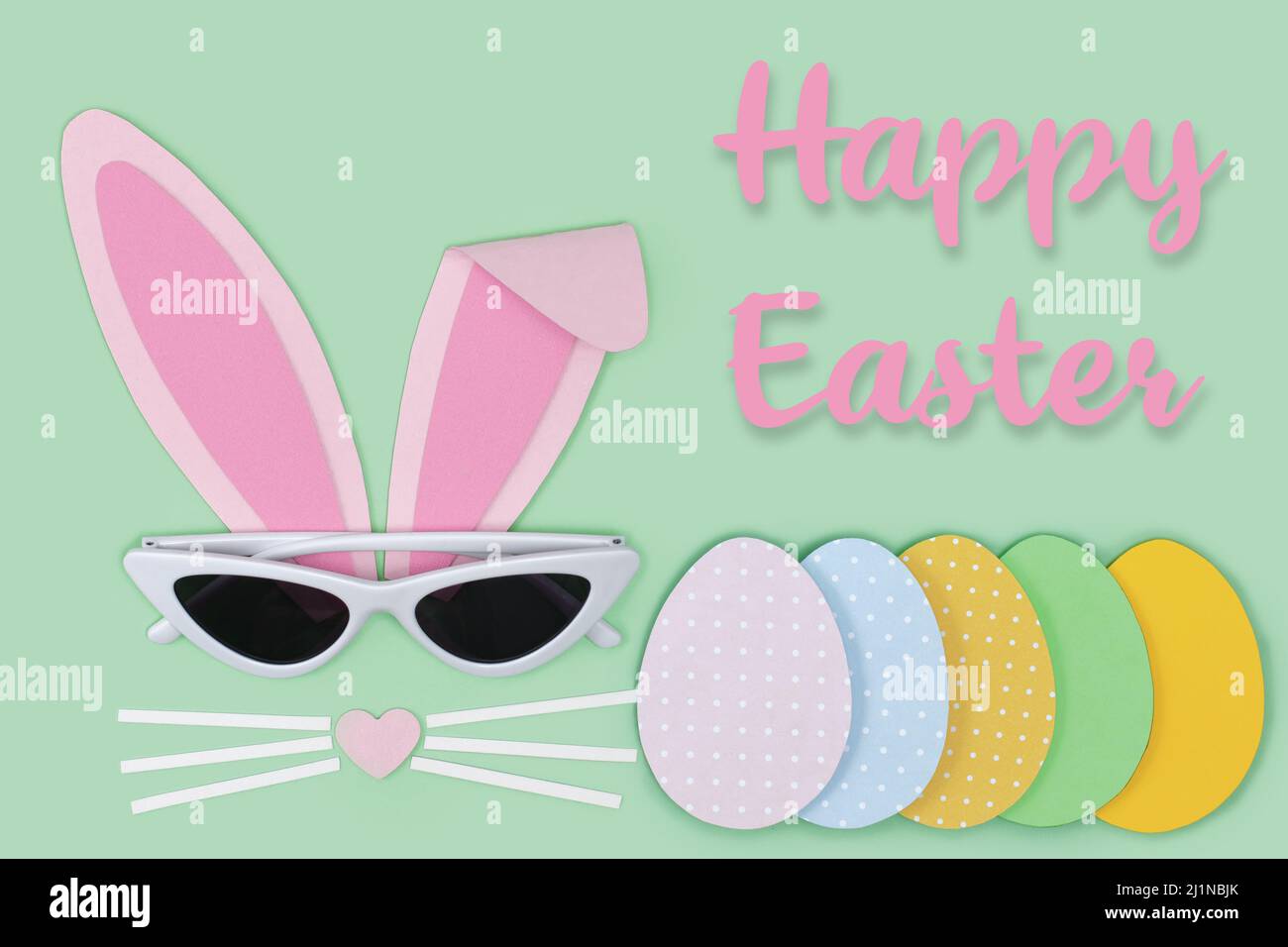 Osterkarte. Hasengesicht aus rosa Papier mit Sonnenbrille und bemalten Ostereiern, die Papier auf blauem Hintergrund ausschneiden. Frohe Ostern Stockfoto