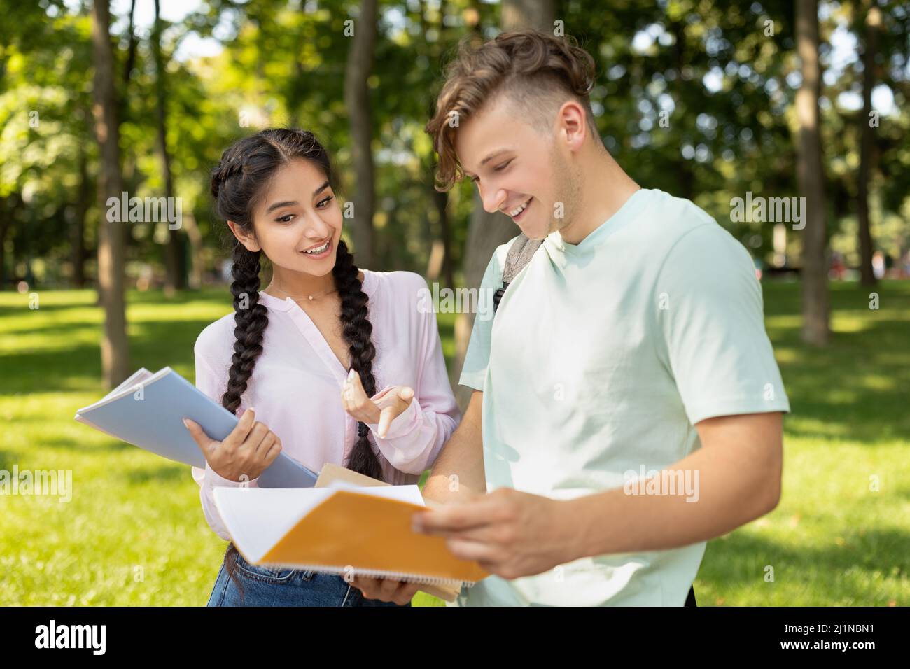 Glückliche, vielfältige Studenten studieren mit Büchern, bereiten sich auf den Unterricht vor, während sie auf dem Universitätscampus im Freien spazieren gehen Stockfoto