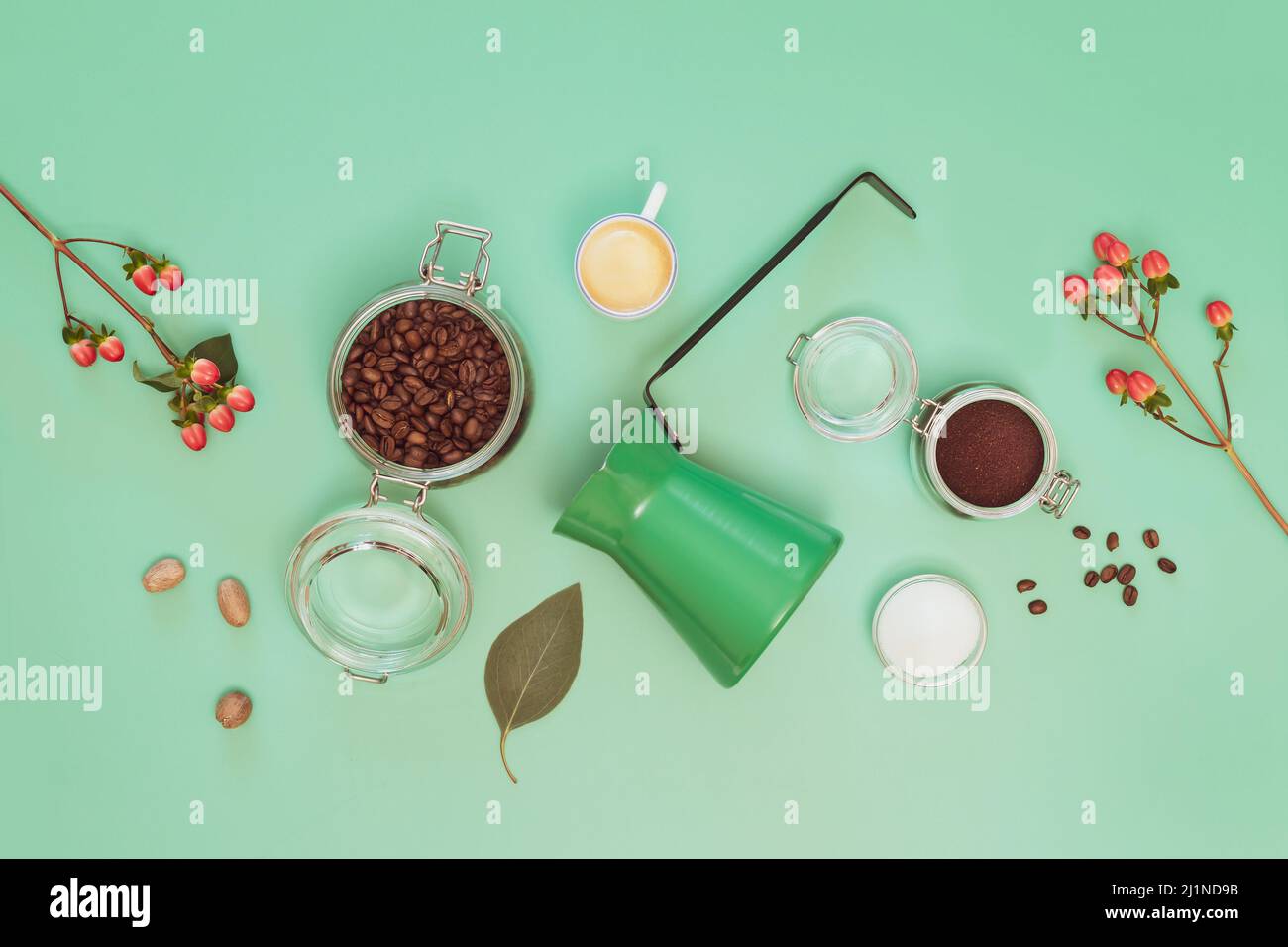 Kaffee zubereiten. Getränkekomposition mit Kaffeebohnen, gemahlenem Kaffee, Zucker, einer Tasse Espresso, einer türkischen Kaffeeschale und Blumen auf minzem Hintergrund. Flach l Stockfoto