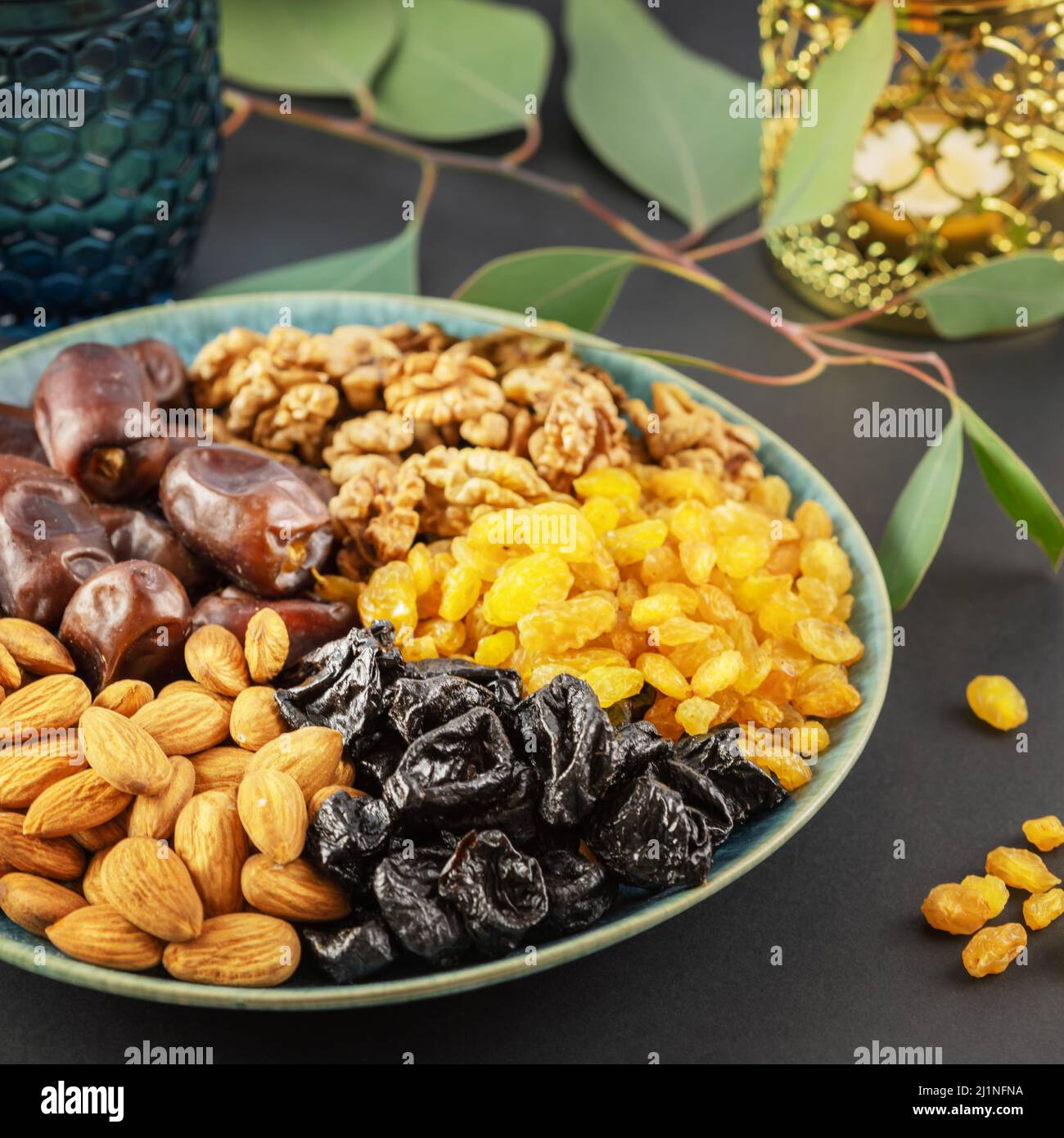 Ramadan-Konzept. Nüsse, getrocknete Früchte und Datteln in der blauen Schale, Glas Wasser und ramadan-Laterne auf schwarzem Hintergrund mit Kopierraum. Arabisches Gericht, s Stockfoto