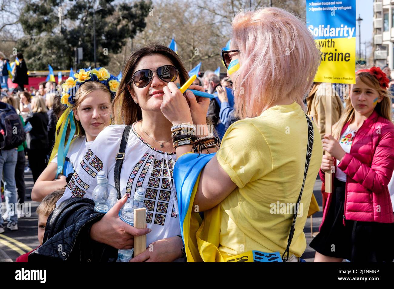 London, 26.. März 2022. Tausende von Menschen treten mit der Ukraine zusammen, marschieren und mahnten im Zentrum von London, um gegen die russische Invasion zu protestieren. Ukrainische Frauen malen Symbole der ukrainischen Flagge auf ihre Wangen, bevor der marsch beginnt. Stockfoto