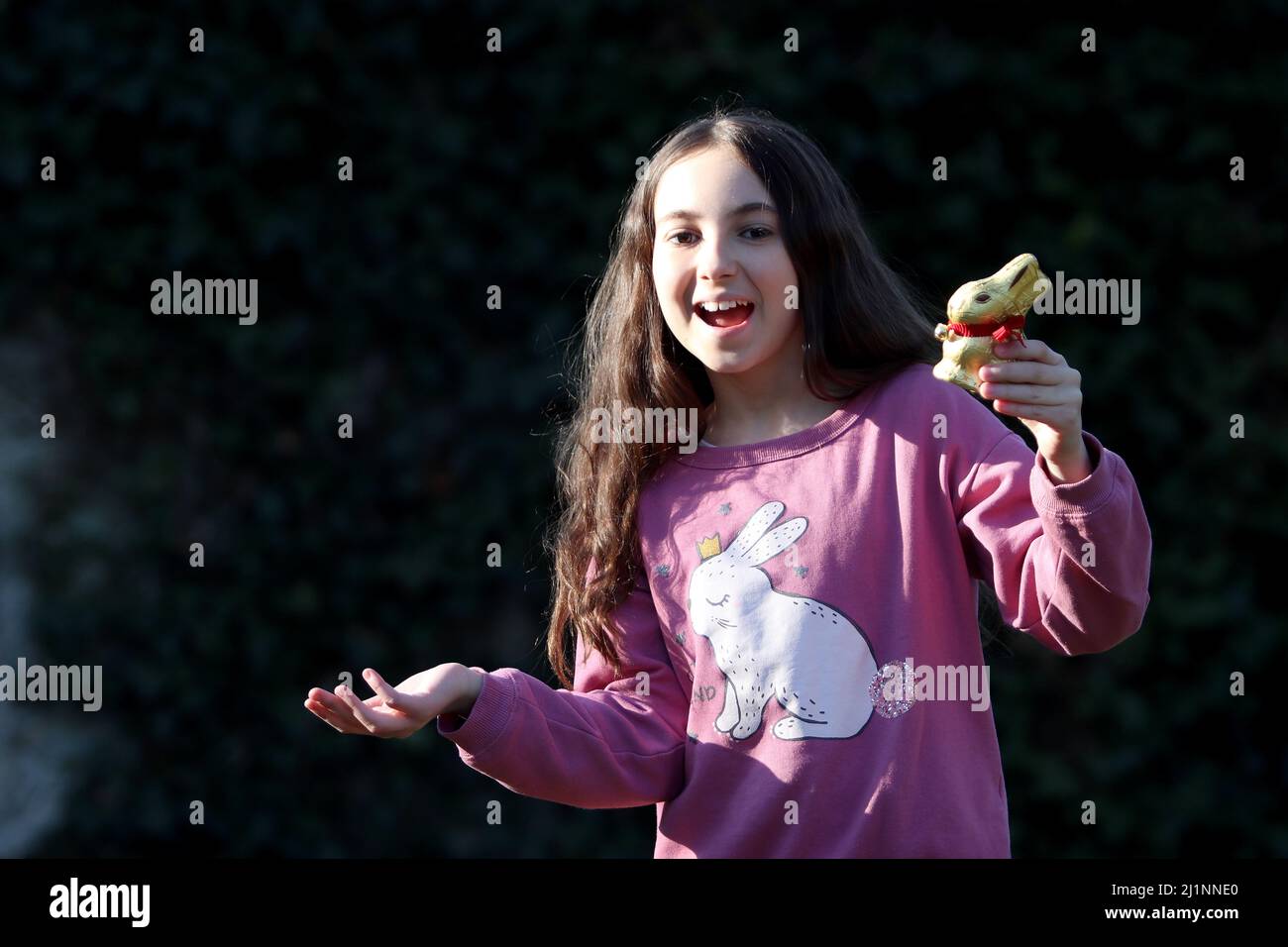 Genf, Schweiz - 03 07 2022 glückliches junges Mädchen mit goldenem osterhase auf Händen. Mädchen feiert Ostern Geschenk im Freien im Park oder Wald.Kleinkind Stockfoto