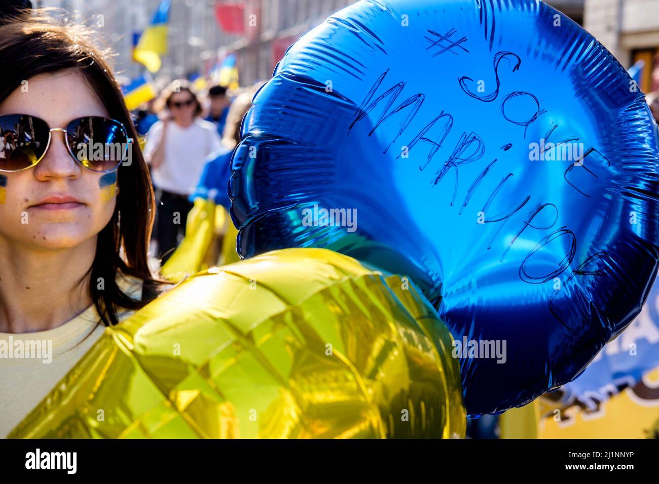 London, 26.. März 2022. Tausende von Menschen treten mit der Ukraine zusammen, marschieren und mahnten im Zentrum von London, um gegen die russische Invasion zu protestieren. Eine junge Frau trägt blaue und goldene Ballons mit einem Plädoyer zur Rettung von Mariupol. Stockfoto