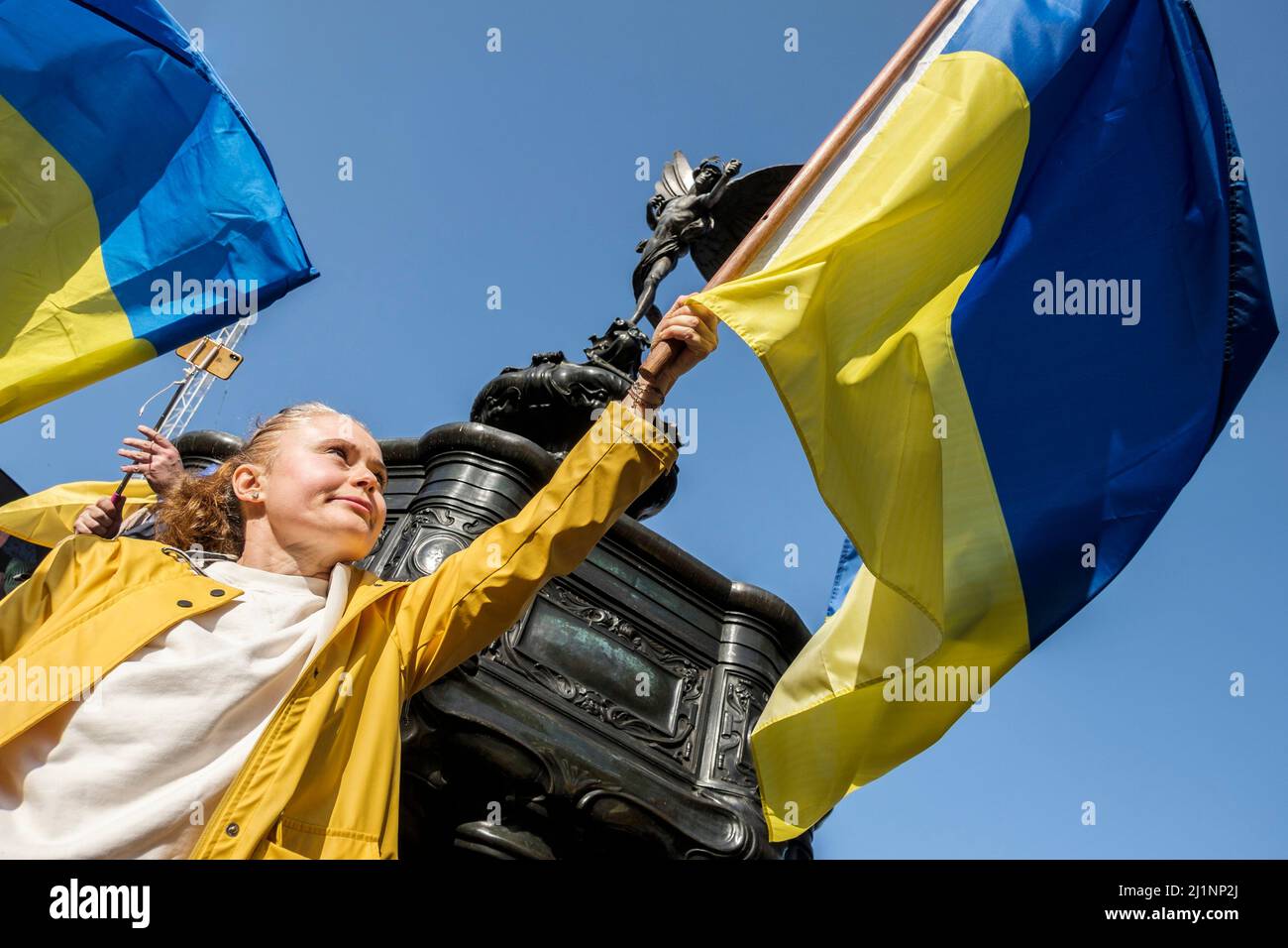 London, 26.. März 2022. Tausende von Menschen treten mit der Ukraine zusammen, marschieren und mahnten im Zentrum von London, um gegen die russische Invasion zu protestieren. Eine junge Frau schwingt unter dem Denkmal im Piccadilly Circus eine ukrainische Flagge. Stockfoto