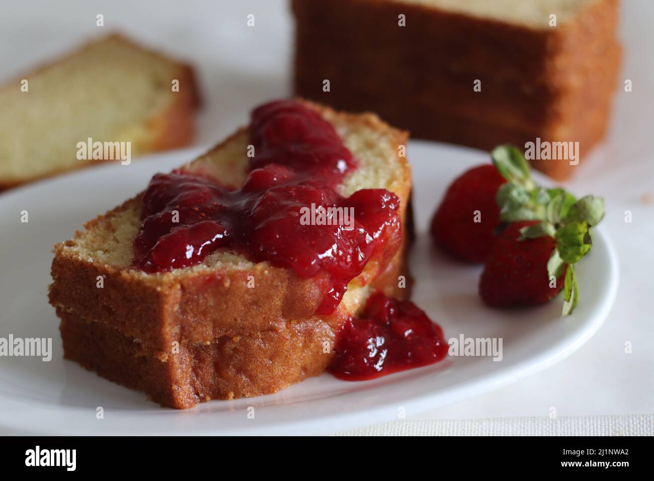 Saure Creme Pfund Kuchen zusammen mit einer Scheibe Pfund Kuchen mit Erdbeersoße Aufstrich. Aufgenommen auf weißem Hintergrund Stockfoto