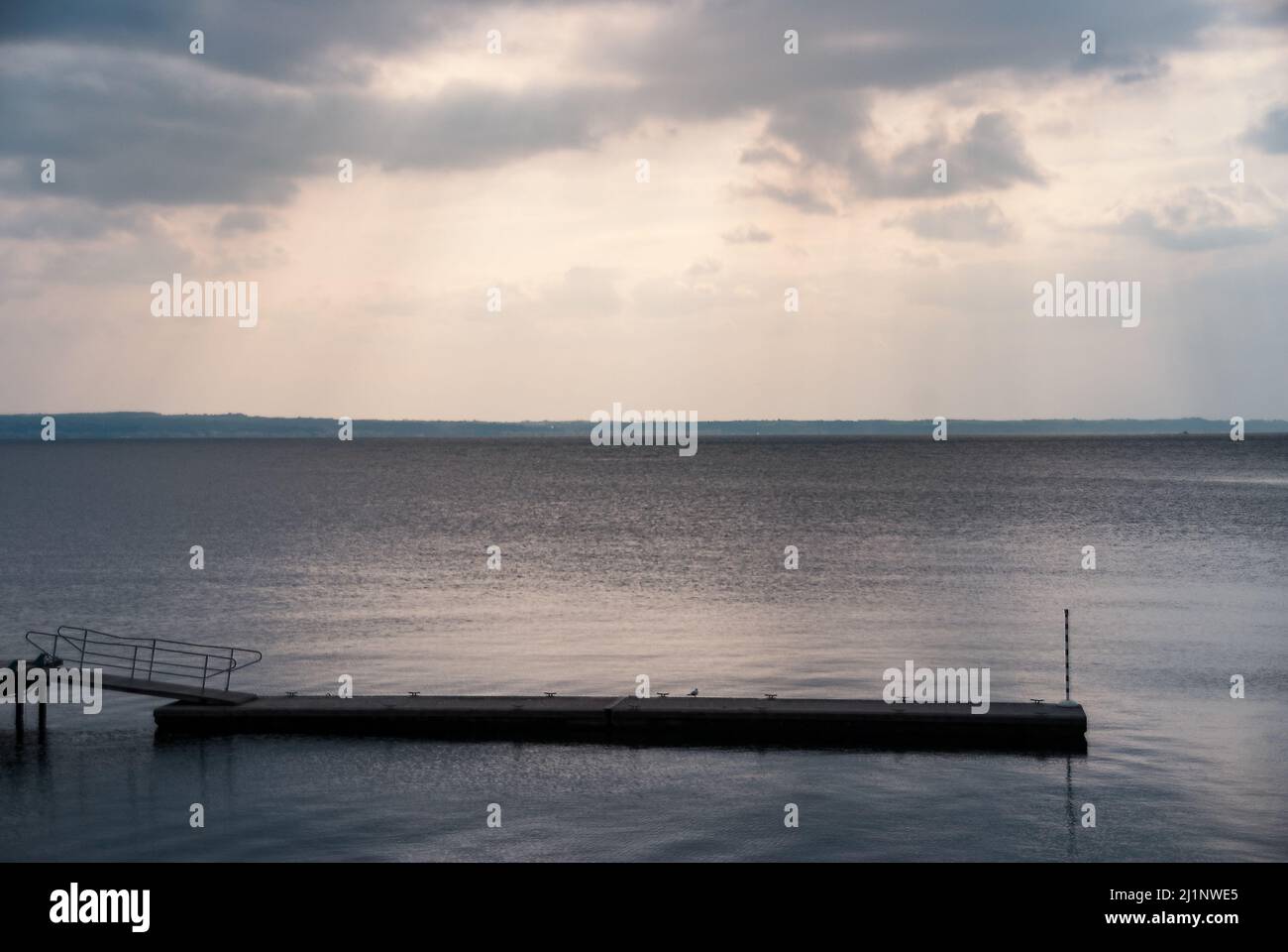 Menschenleerer Pier unter den Strahlen der untergehenden Sonne, die in der Dämmerung durch Wolken spätet Stockfoto