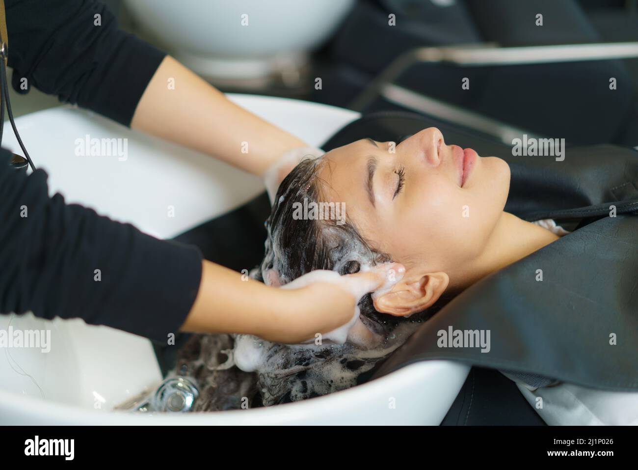 Friseur ist die Anwendung Shampoo und massieren Haar eines Kunden. Frau, die ihre Haare in einem Friseursalon gewaschen. Stockfoto