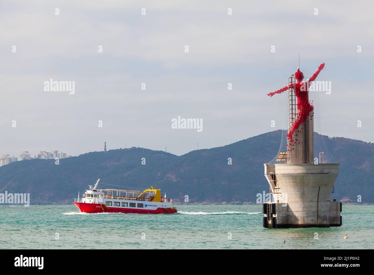 Busan, Südkorea - 17. März 2018: Fähre mit Haeundae Cruise segelt an einem sonnigen Tag in der Nähe der roten Leuchtturmskulptur Stockfoto