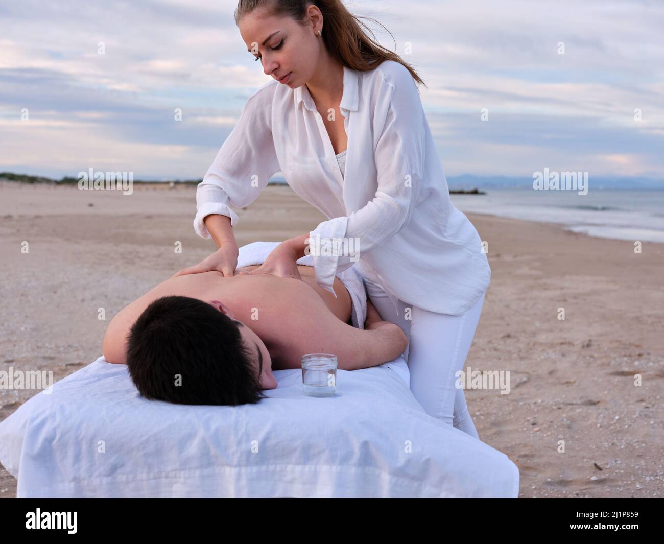 Eine junge Chiromassage-Therapeutin, die einem jungen Mann auf einem Massageliege am Strand von Valencia eine Massage auf den Rücken gibt. Stockfoto