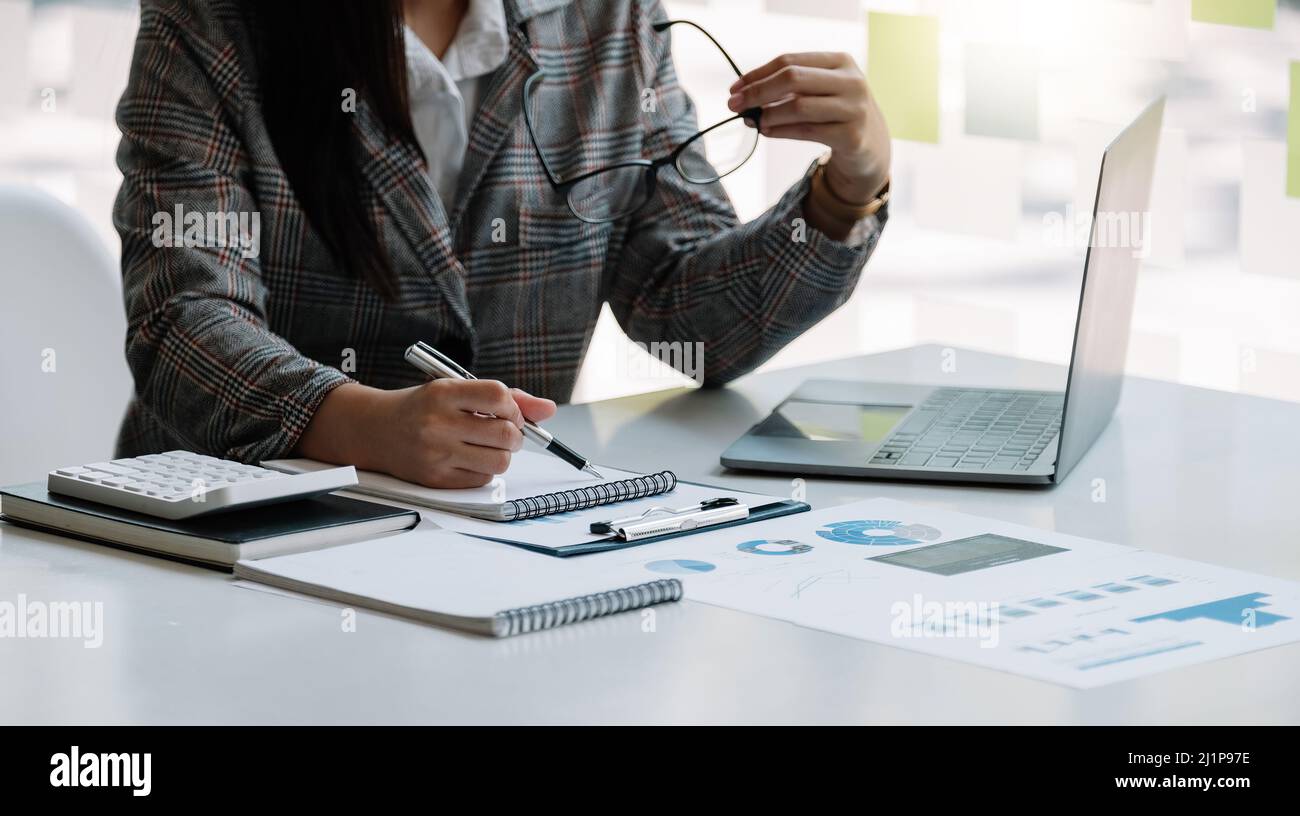 Geschäftsfrau nimmt sich Notizen und benutzt Taschenrechner und Laptops auf einem weißen Tisch. Rechnungslegungskonzepte Stockfoto