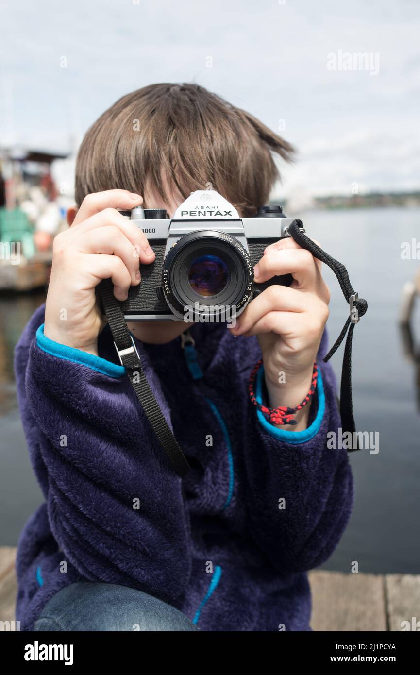 Ein kleiner Junge versucht zu lernen und mit der Filmkamera zu fotografieren. Junge mit Filmkamera Fotografie lernen. Pentax Filmkamera und ein Kind. Talentiertes Kind. Stockfoto