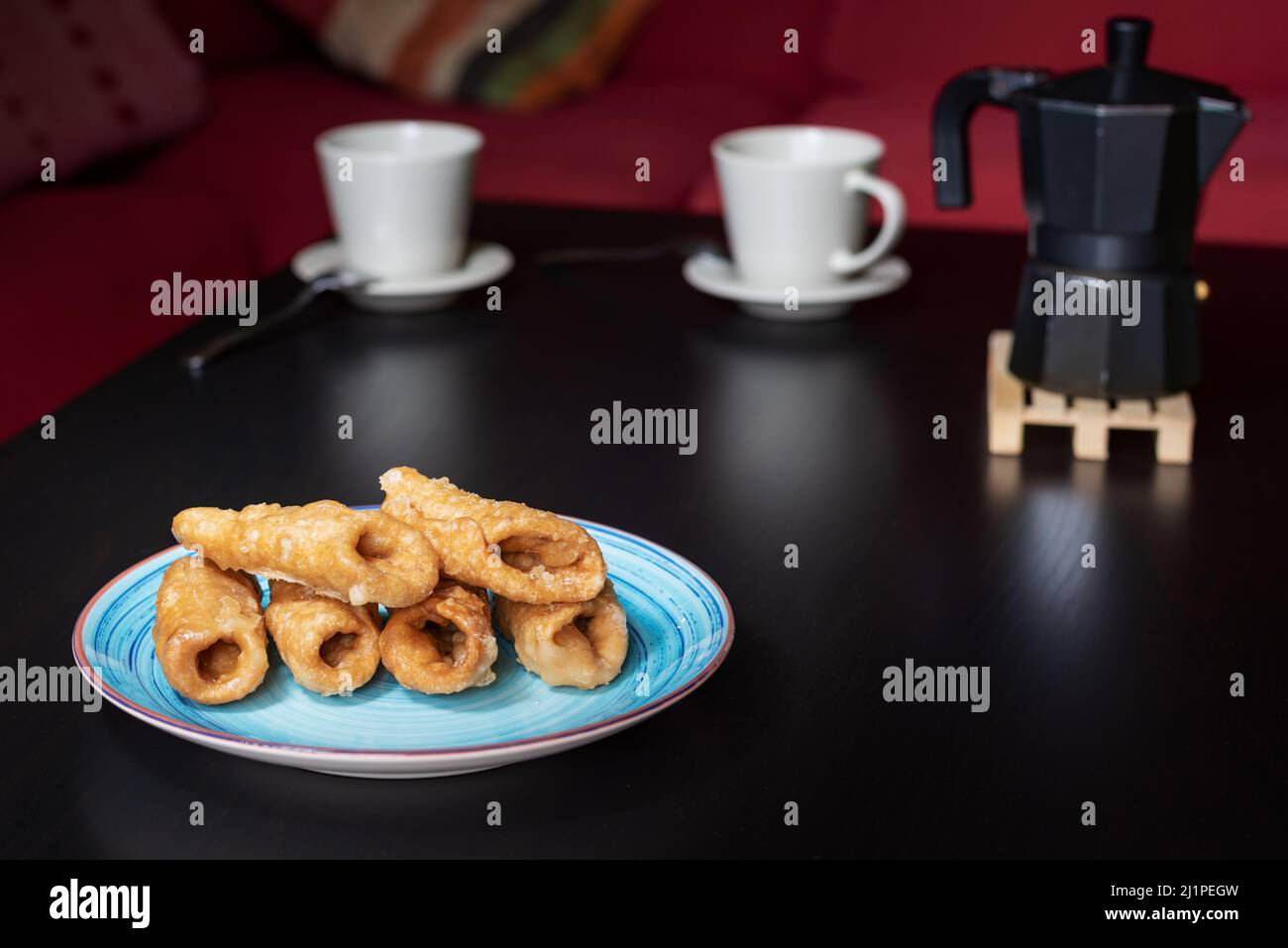 Teller mit pestiños auf einem Tisch mit Tassen Kaffee neben einer Kaffeedose. Stockfoto