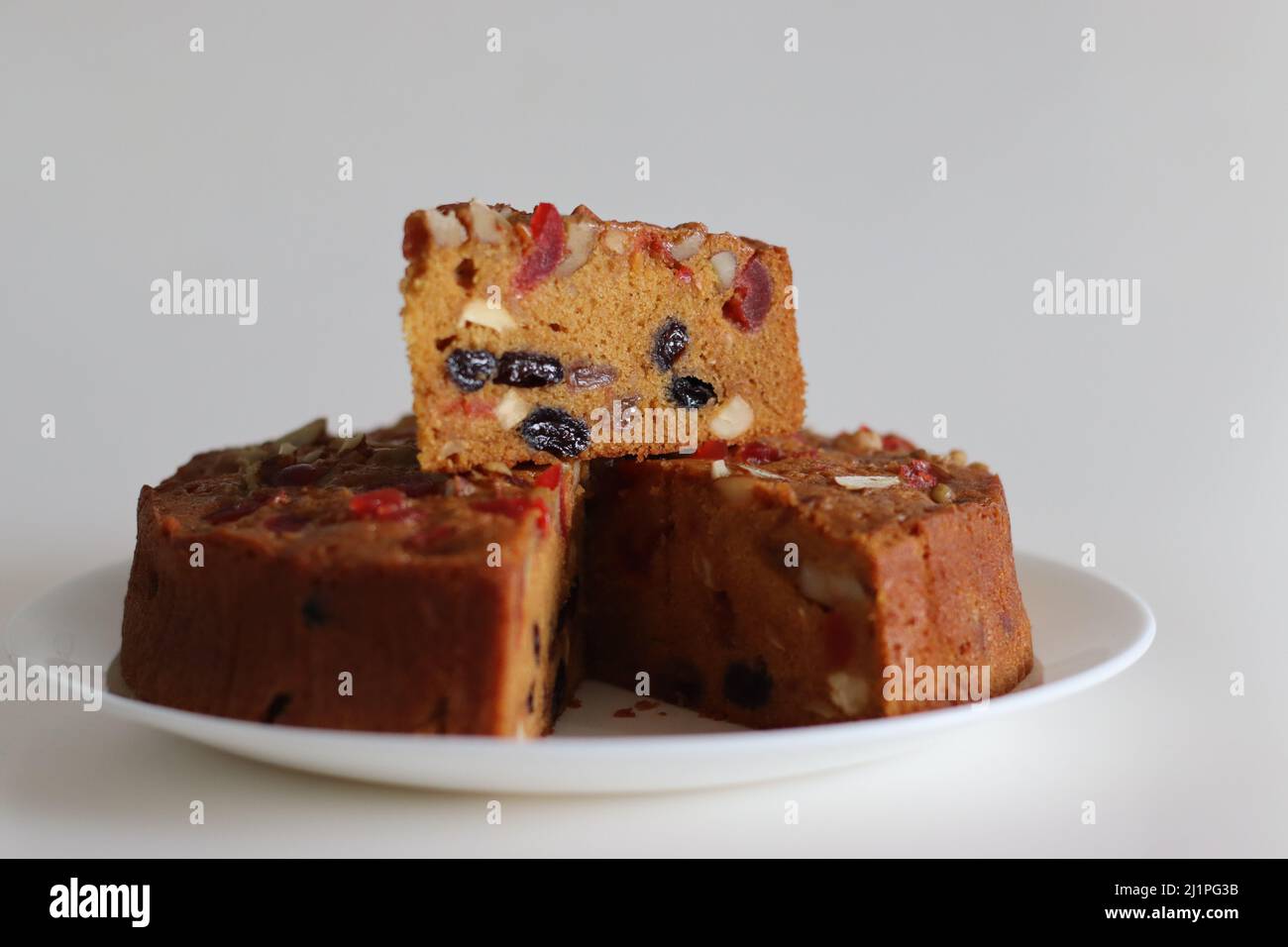 Obstkuchen in Scheiben mit Rum getränkten Früchten und Nüssen, die für weihnachten zubereitet werden. Aufgenommen mit Weihnachtsbaum, Kiefernkiefern, dekorativen Bändern im Hintergrund Stockfoto