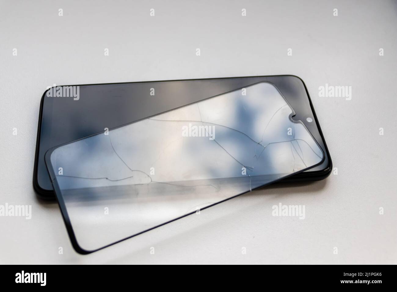 Der zerbrochene Schutzschild auf einem schwarzen Smartphone zeigt Display-Schutz und bruchsichere transparente Geräteprotektoren für die Crashsicherheit von Mobiltelefonen Stockfoto
