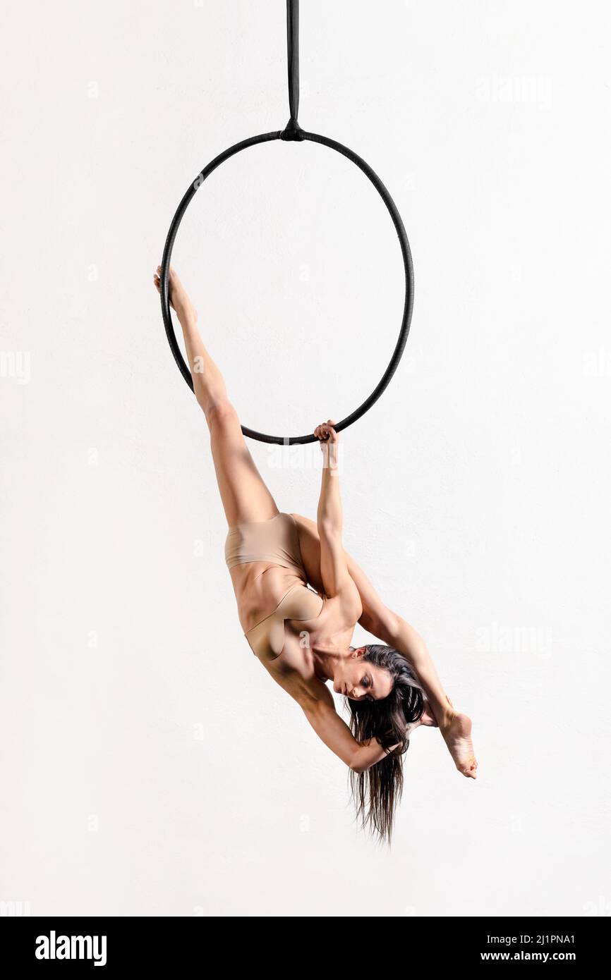 Flexible weibliche Turnerin, die akrobatische Splitten auf einem Reifen unter der Decke auf weißem Hintergrund aufführt Stockfoto