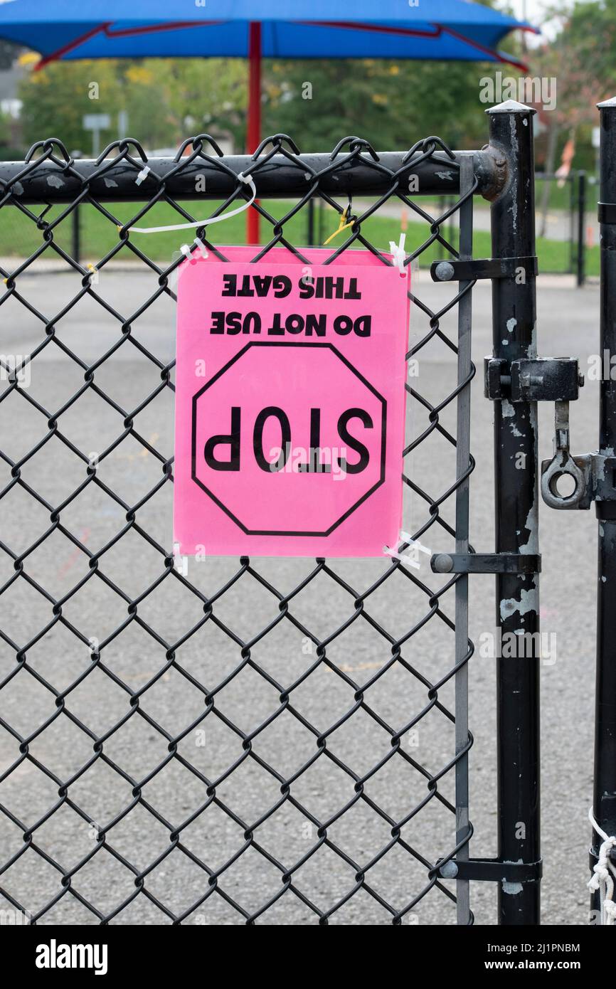 Ein auf dem Kopf stehendes „Stop“-Schild „Don’t Use This Gate“, das auf Kettengliederzäunen in einem Schulhof, Ontario, Kanada, angebracht ist - Stock-Fotografie Stockfoto