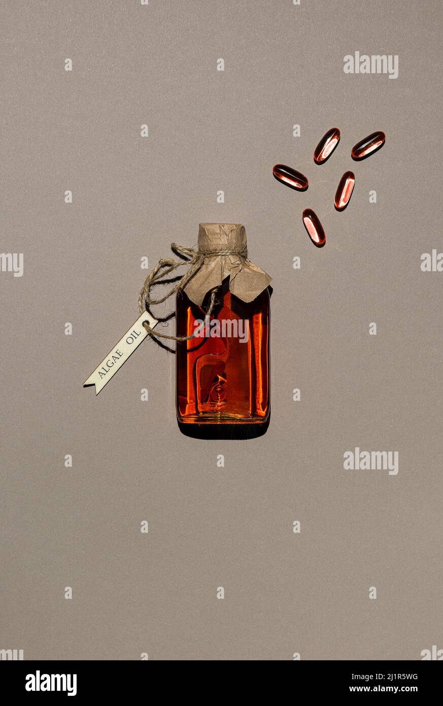 Transparenter Behälter, gefüllt mit Öl auf Algenbasis und wenigen Gelatineölkapseln. Glasflasche ist mit Jute-Gewinde mit Holzetikett gebunden. Braunes Papier b Stockfoto