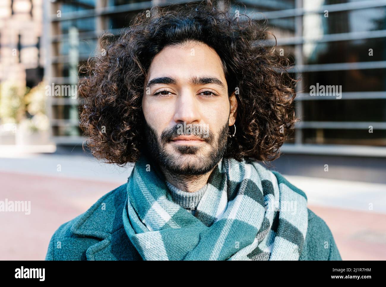 Stadtportrait des jungen lockigen Mannes mit Bart auf der Straße posiert Stockfoto