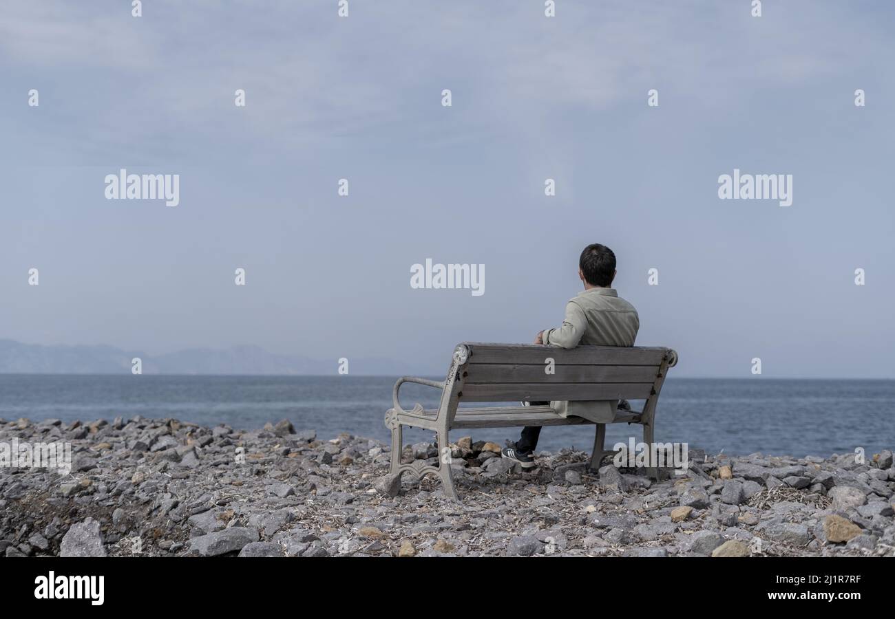 Deprimierter einsamer Mann, der auf einem Ufer am Meer sitzt. Stockfoto