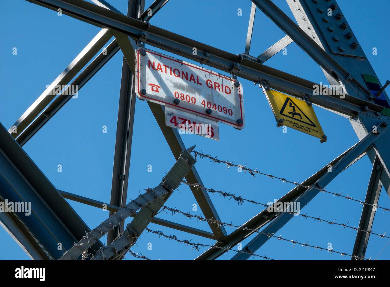 Unterer Abschnitt eines Sendeturms mit Warnschild „Gefahr des Todes“ und kletterfester Stacheldraht-Barriere gegen einen blauen Himmel Stockfoto