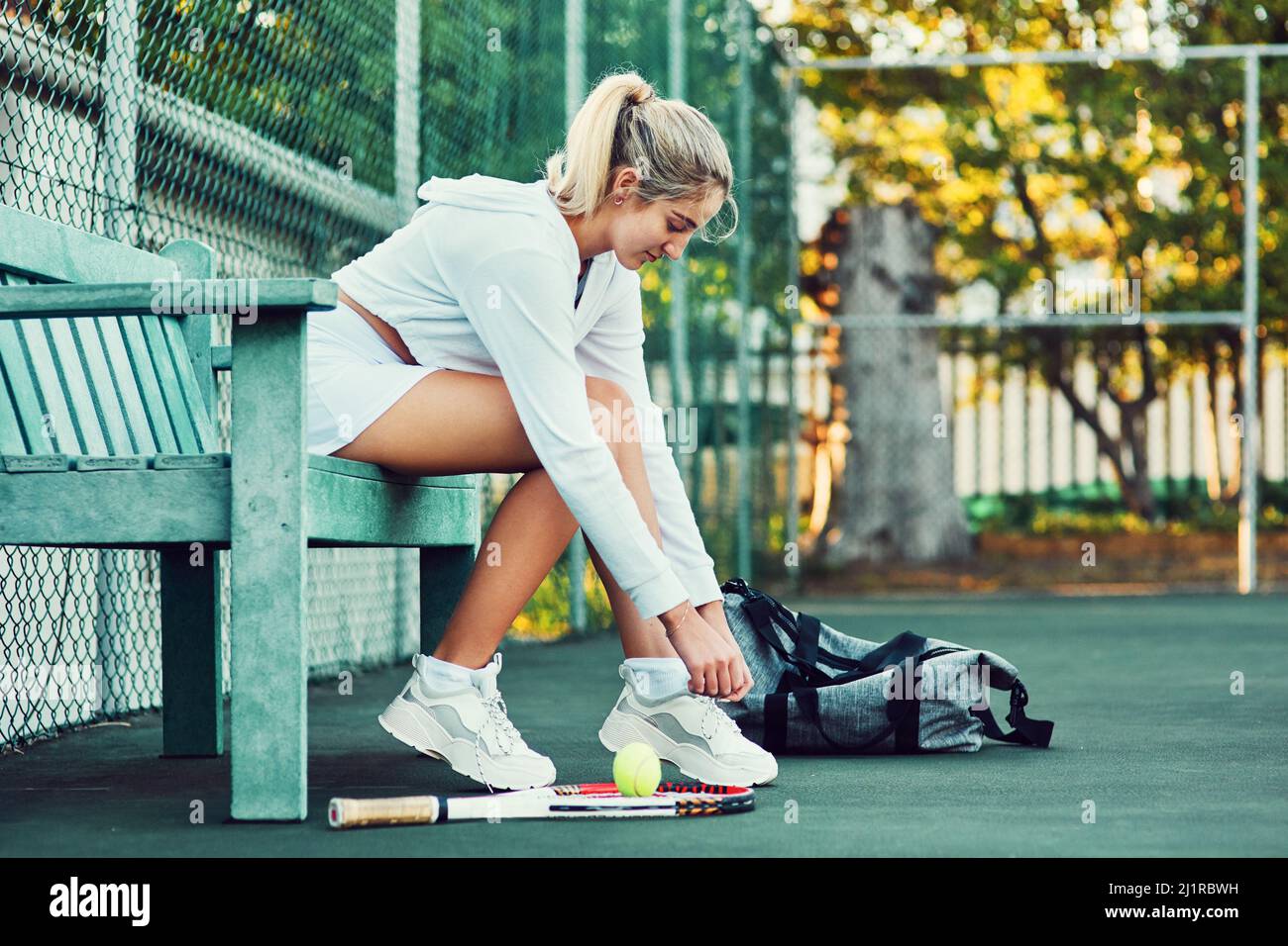 Sich auf ein großes Spiel einstellen. Aufnahme einer sportlichen jungen Frau, die ihre Schnürsenkel festbindet, während sie auf einer Bank auf einem Tennisplatz sitzt. Stockfoto