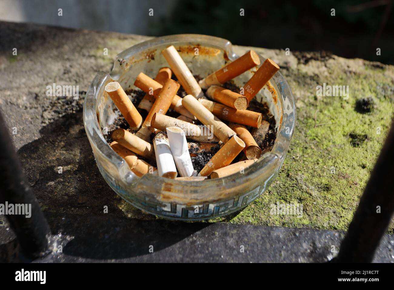 Eine große Anzahl von Zigarettenenden, die in einem runden Glasaschenbecher außen an einer Wand stehen Stockfoto