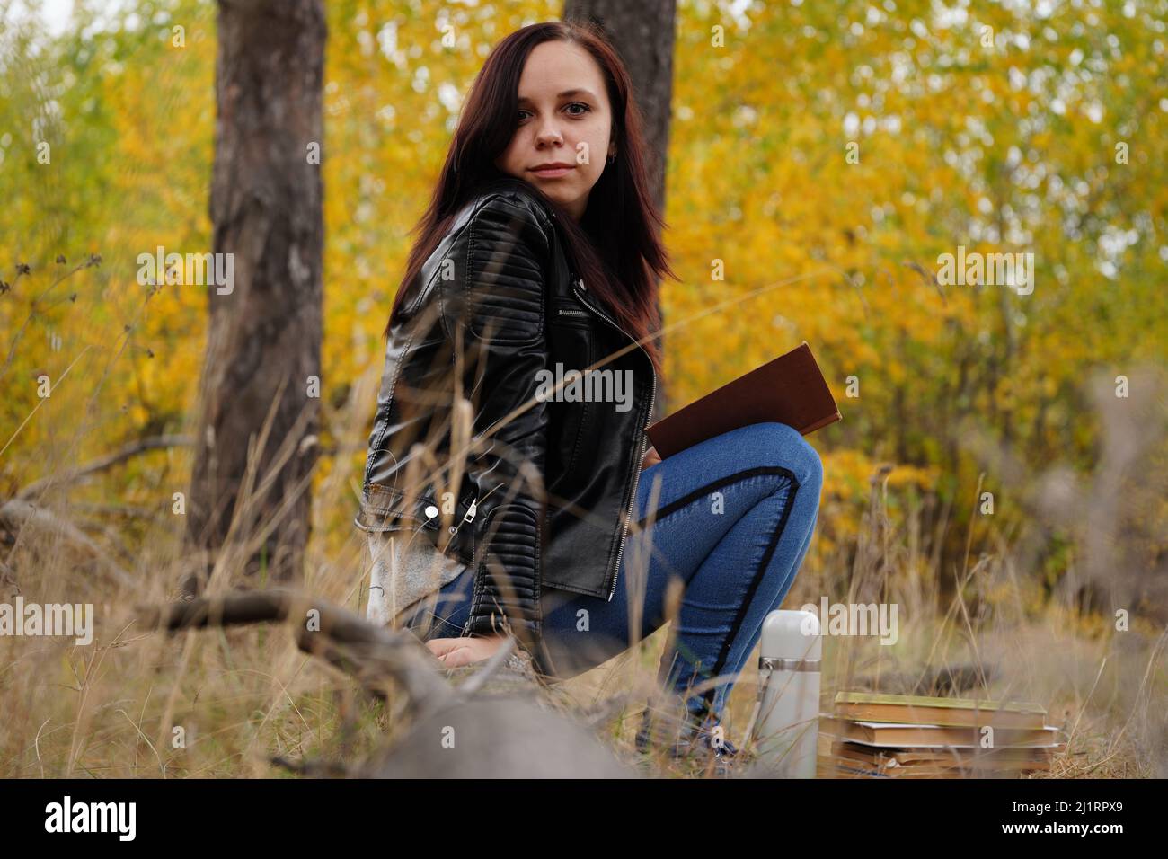 Eine junge, schöne Frau mit langen, dunklen Haaren in legerer Kleidung sitzt auf einem Holzbuch und liest ein Buch Stockfoto