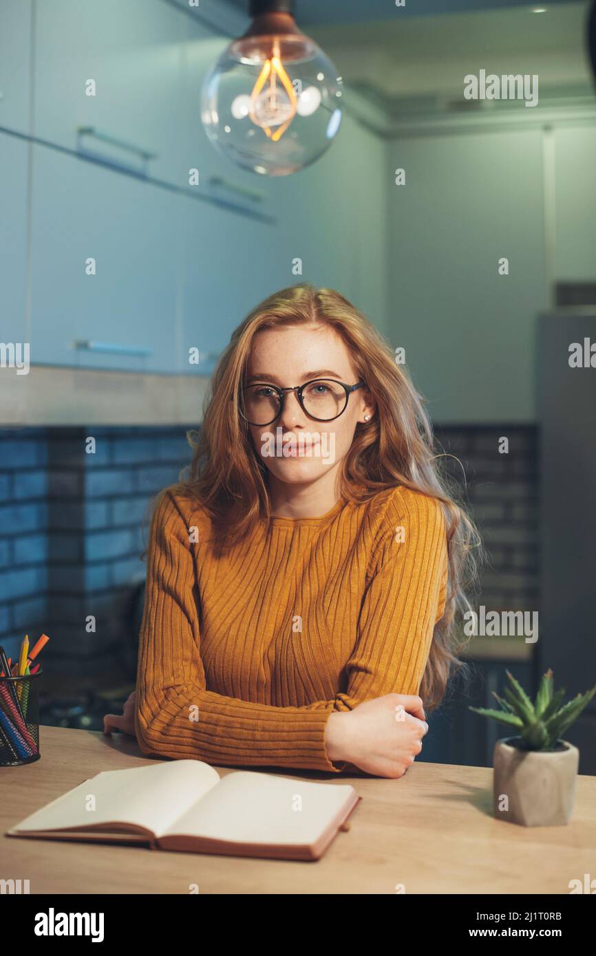 Müde rothaarige Studentin sitzt an einem Tisch mit Lehrbüchern Blick auf Kamera Vorbereitung für College-Prüfungen. Wunderschönes Porträt. Bildung Stockfoto