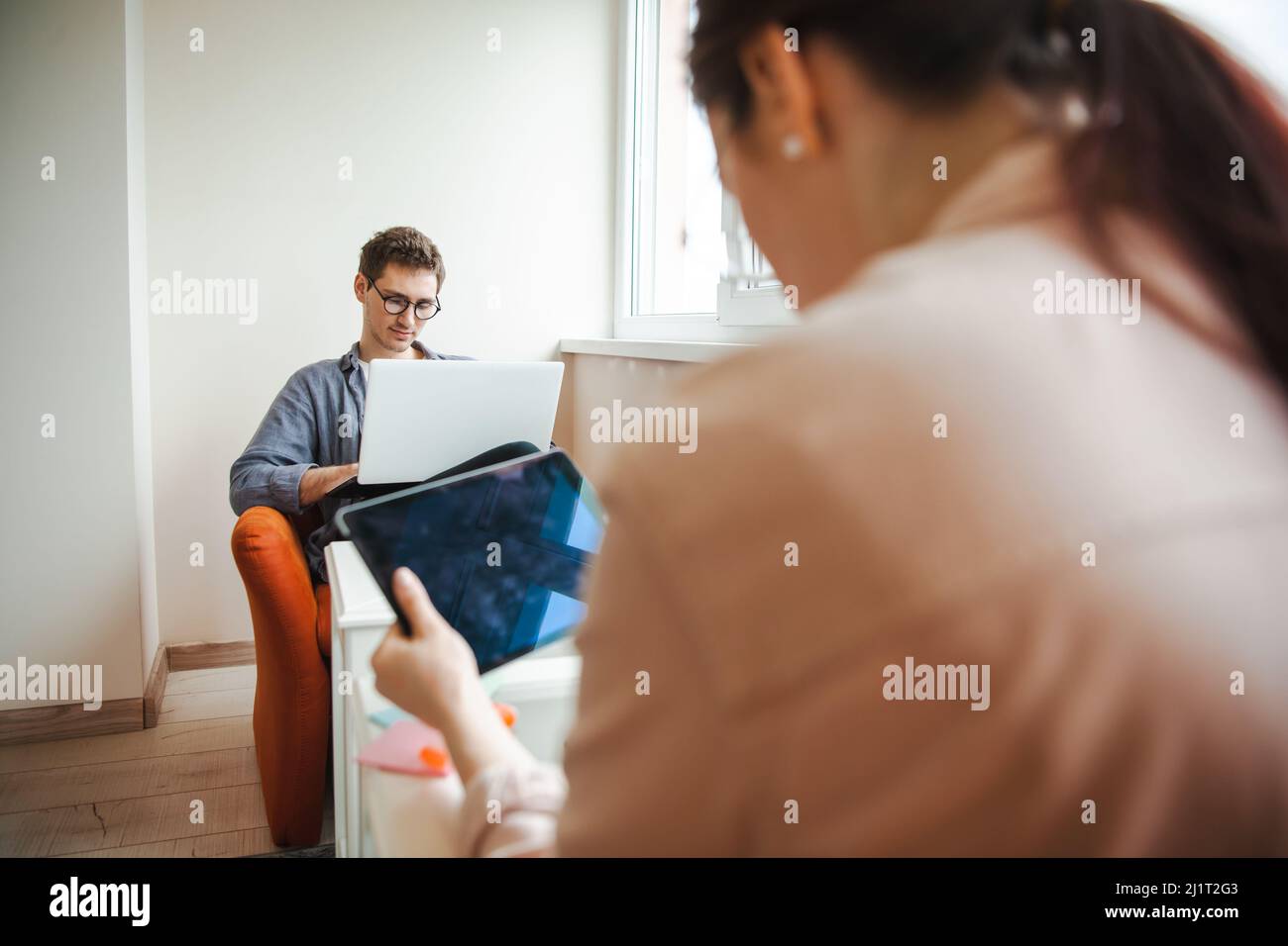 Paar mit Laptops arbeiten von zu Hause aus im Wohnzimmer mit sozialer Distanz wegen der Pandemie-Situation. Gesunder Lebensstil. Unternehmenstechnologie. Stockfoto