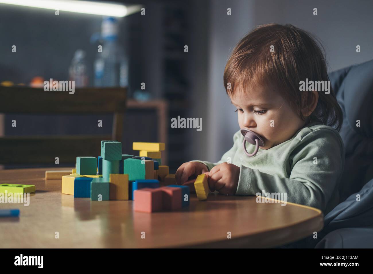 Kleines Mädchen, das auf dem Hochstuhl sitzt, während es zu Hause mit hölzernen Spielzeugblöcken spielt. Portrait für Lifestyle-Design. Entwicklung des Babys. Stockfoto