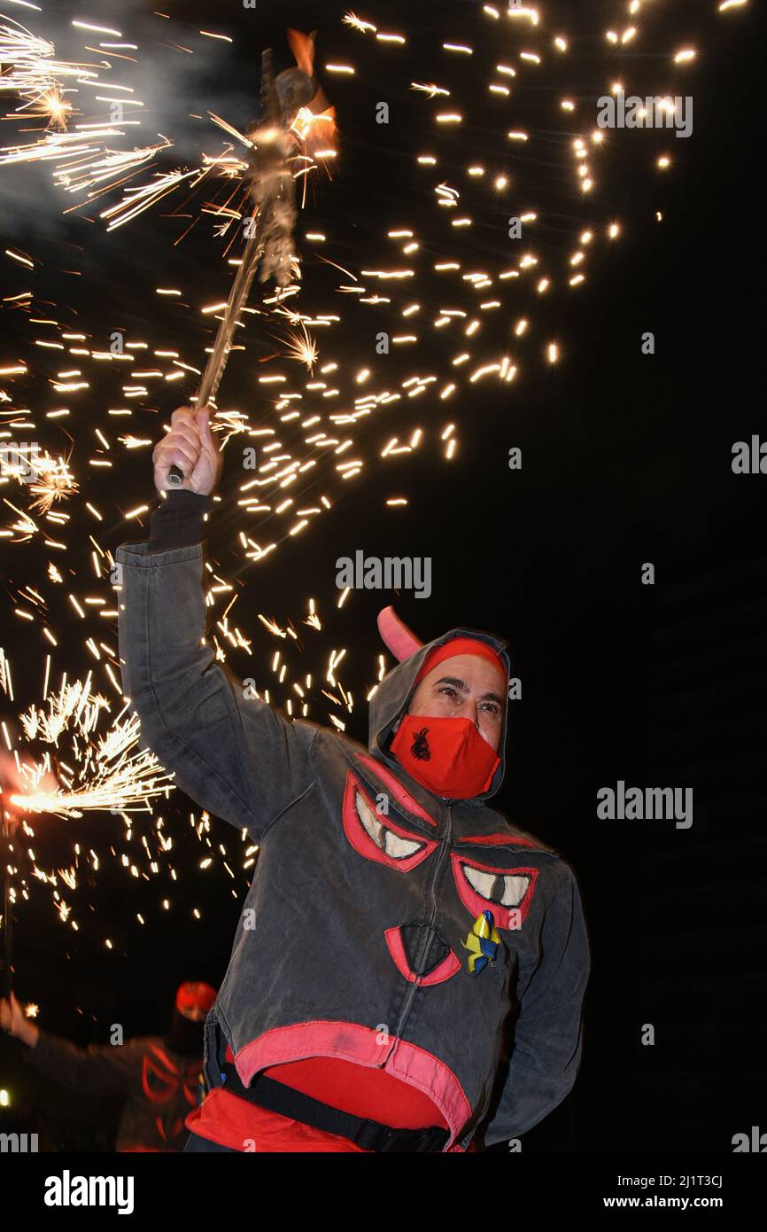 Ein als Teufel getarnter Demonstrator, der während der pyrotechnischen Demonstration in Solidarität mit den ukrainischen Flüchtlingen in Vendrell unter den Funken des Feuers gesehen wurde. Die Vereinigung „DRAC de FOC El Cabrot de El Vendrell“ (Feuerdrache) handelt in einer pyrotechnischen Darstellung in Solidarität und Unterstützung für Menschen ukrainischer Nationalität, die aufgrund der Invasion Russlands in der Ukraine in Hotels und kommunalen Hostels in der Stadt Vendrell Flüchtlinge sind, Die Aufführung von Feuerparaden ist eine katalanische Tradition, die jedes Jahr in Städten und Gemeinden stattfindet. Stockfoto