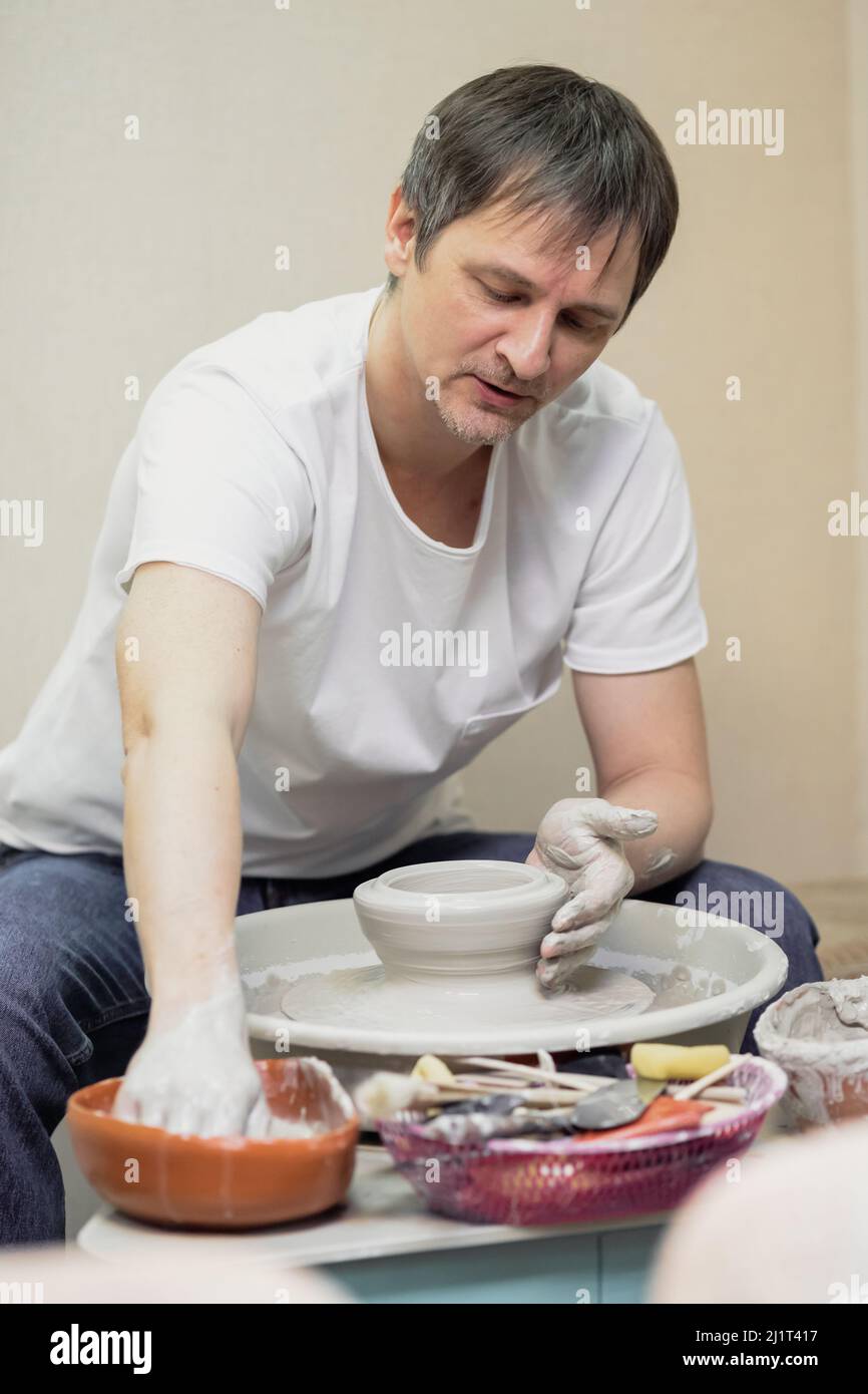 Ein Mann in einem weißen T-Shirt und Jeans, in einer Töpferwerkstatt, der hinter einem Töpferrad arbeitet Stockfoto