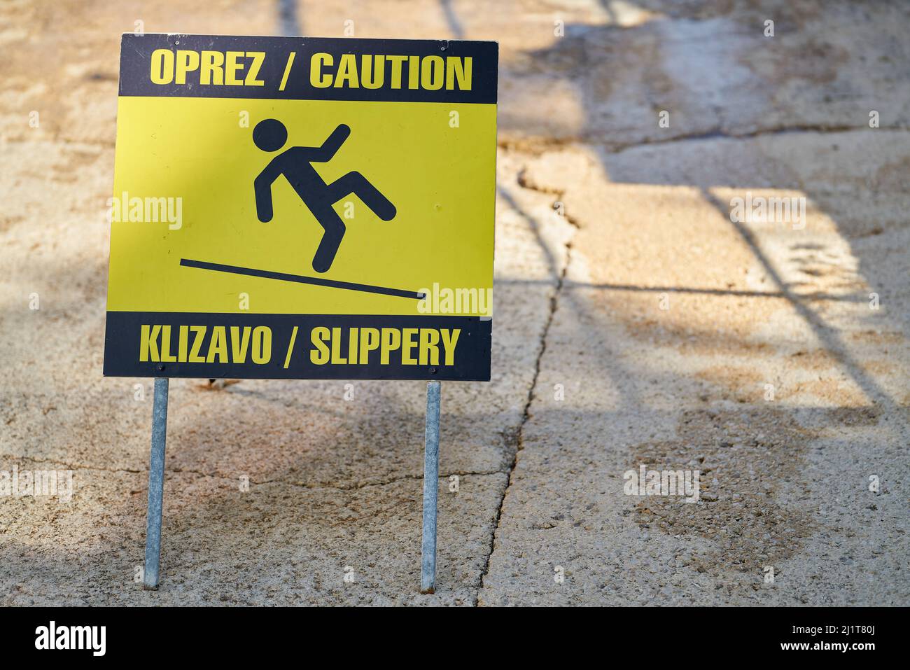 Schild mit der Aufschrift Achtung rutschig in kroatischer und englischer Sprache in der Altstadt von Krk in Kroatien Stockfoto