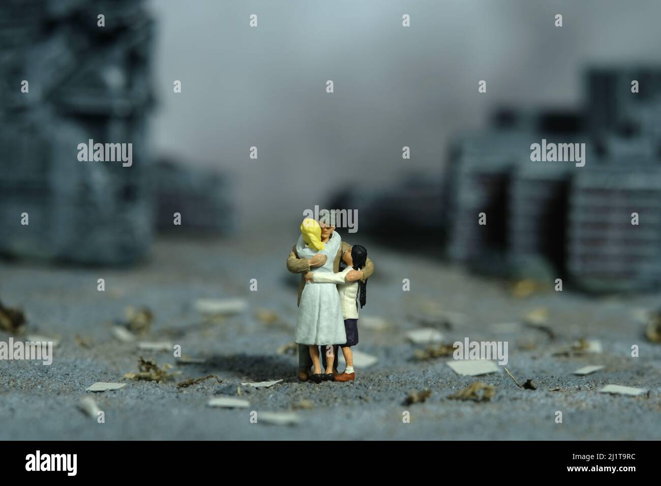 Miniatur Menschen Spielzeug Figur Fotografie. Konzept für Familientreffen. Der Vater umarmte seine Frau und seine Tochter mitten in der zerstörten Stadt. Bild pho Stockfoto