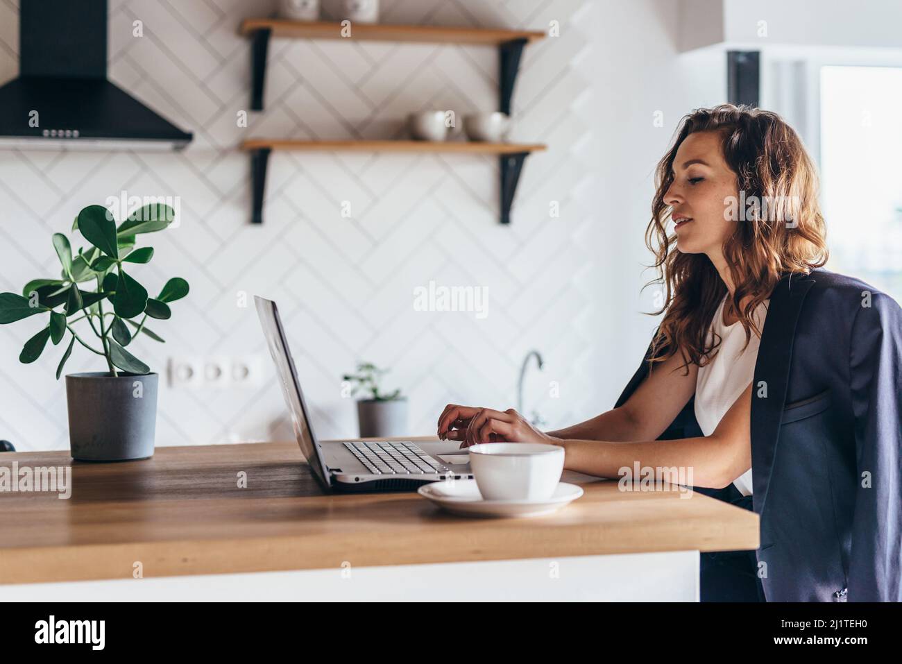 Junge Frau, die vor einem offenen Laptop sitzt und zu Hause arbeitet. Stockfoto