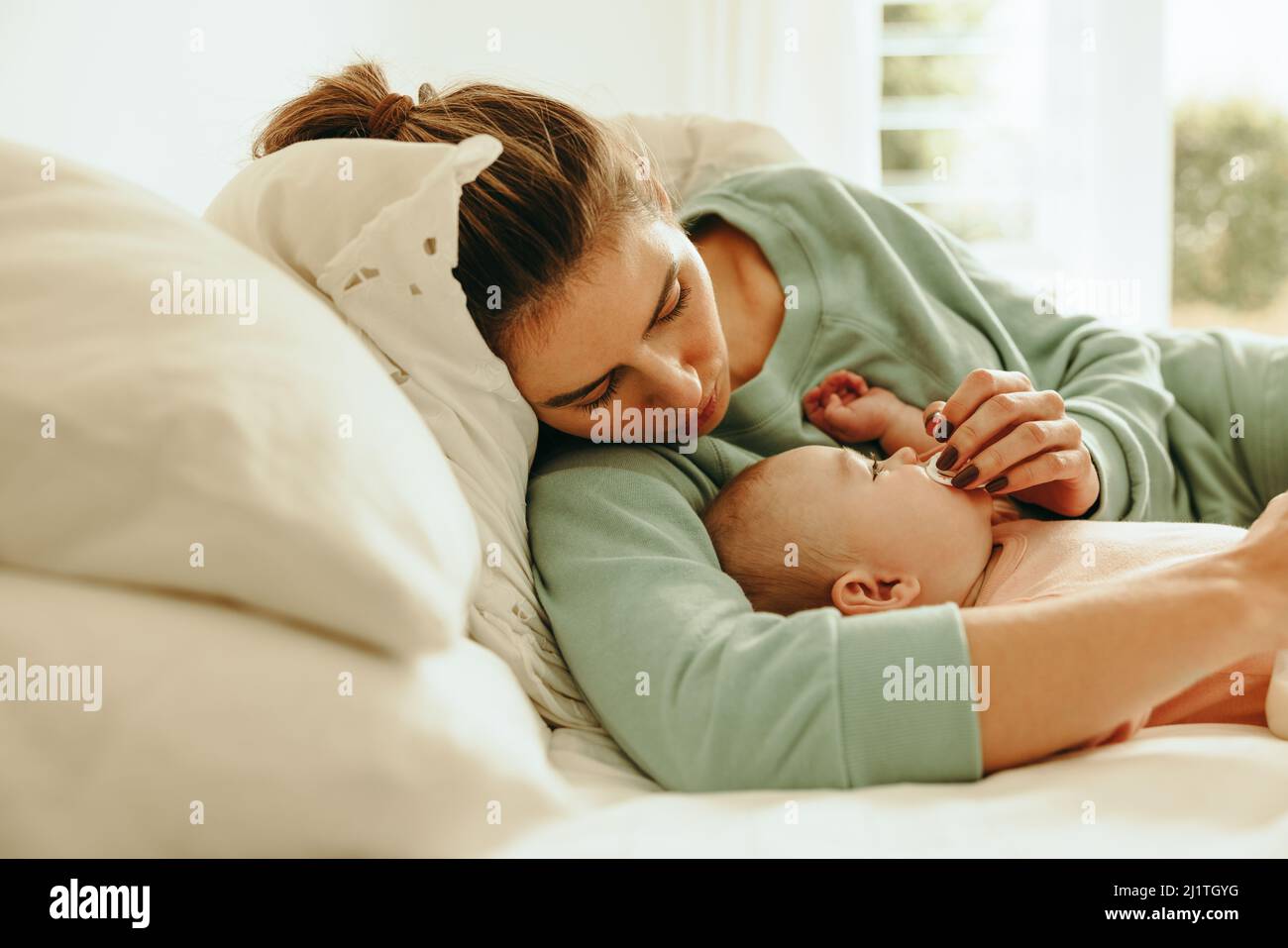 Neue Mutter gibt ihrem Baby einen Schnuller zum Ansaugen. Liebevolle junge Mutter, die sich um ihr Baby kümmert, während sie zu Hause im Bett liegt. Alleinerziehende Mutter versucht, ein Nickerchen zu machen Stockfoto