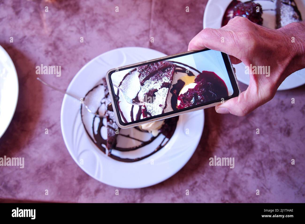 Hand des Mannes hält Handy und schießt Schokoladenkuchen Stockfoto